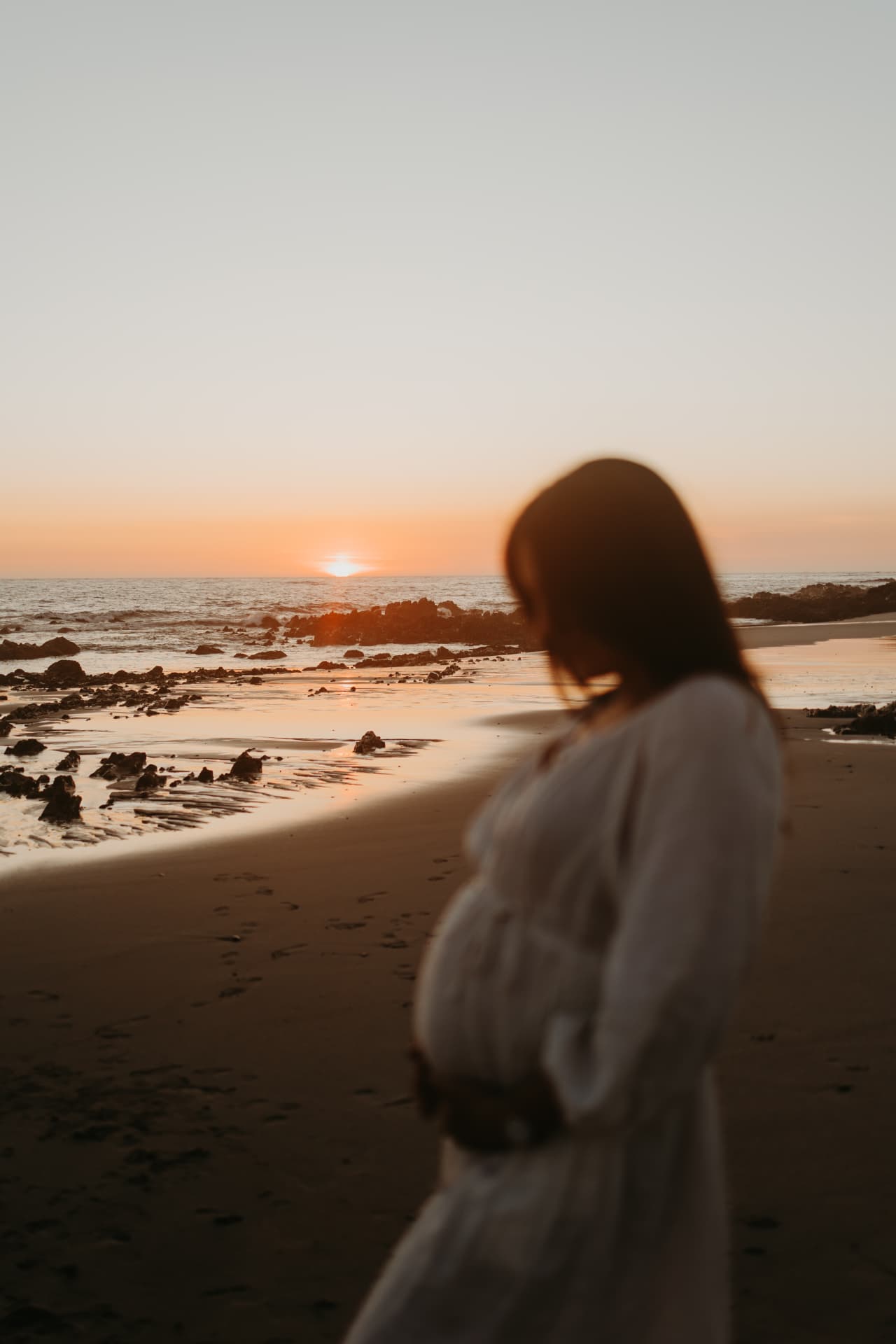 Stefani am Meer im Abendlicht, die Hände auf dem Babybauch